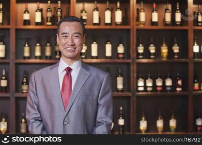 Smiling Businessman Standing by Wine Bottles, Portrait