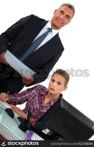Smiling businessman standing over his overworked assistant
