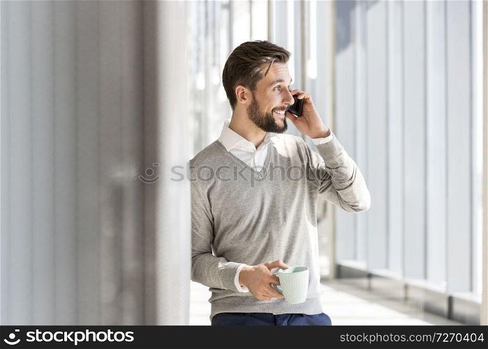 Smiling businessman talking on mobile phone while having coffee at office