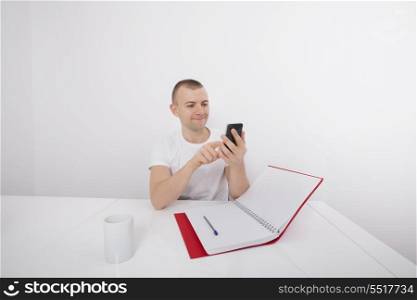 Smiling businessman text messaging on cell phone at desk