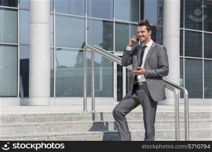 Smiling businessman using cell phone while standing on steps outside office