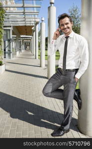 Smiling businessman using mobile phone while leaning on column outside office