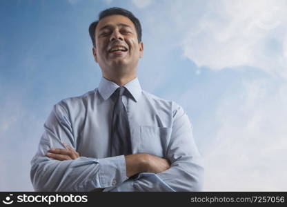 Smiling businessman with eyes closed standing with his arms crossed with sky in the background