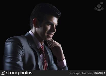 Smiling businessman with hand on chin looking away against black background
