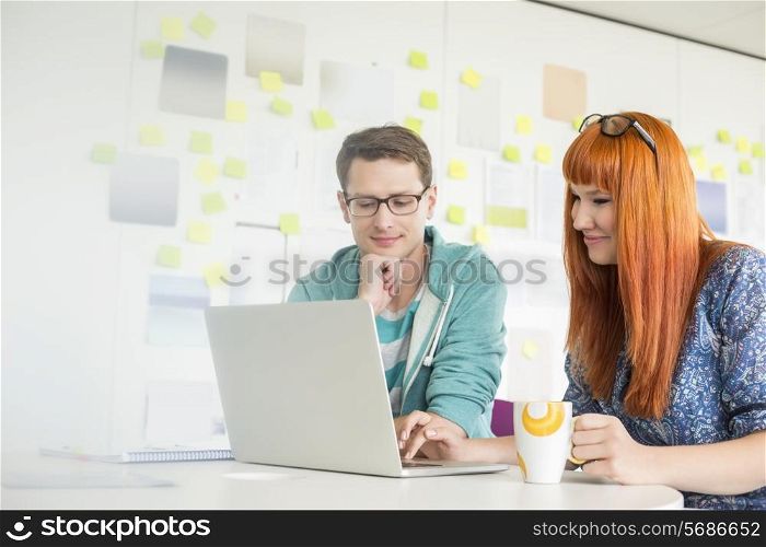 Smiling businesspeople using laptop at desk in creative office
