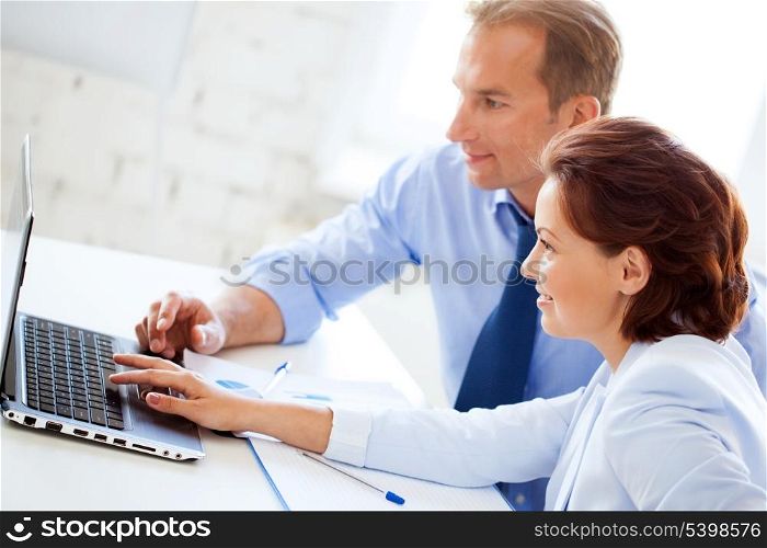smiling businesswoman and businessman working with laptop in office