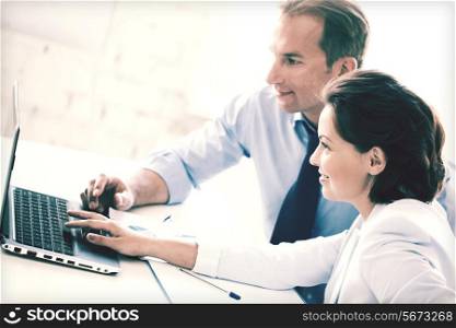 smiling businesswoman and businessman working with laptop in office