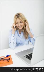 Smiling businesswoman answering cell phone in office