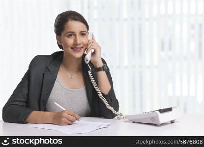 Smiling businesswoman answering telephone at office desk