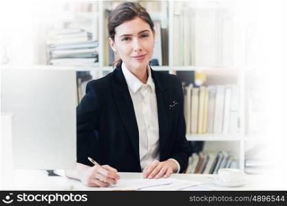 Smiling businesswoman at office. Portrait of smiling businesswoman looking at camera and smiling while working with documents at office in front of computer