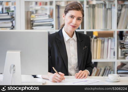 Smiling businesswoman at office. Portrait of smiling businesswoman looking at camera and smiling while working with documents at office in front of computer