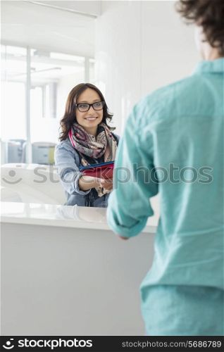 Smiling businesswoman handing over to male colleague at counter in creative office