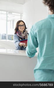 Smiling businesswoman handing over to male colleague at counter in creative office