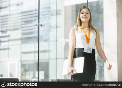 Smiling businesswoman holding laptop while standing in office
