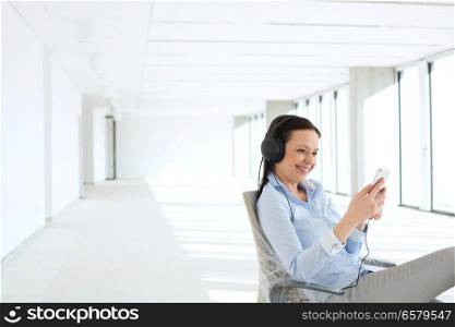 Smiling businesswoman listening music through headphones in empty office