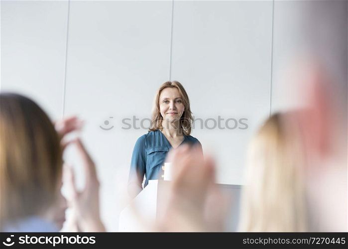 Smiling businesswoman looking at colleagues clapping in conference