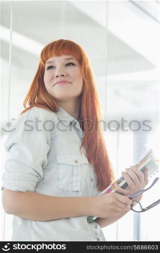 Smiling businesswoman looking away while holding files in creative office