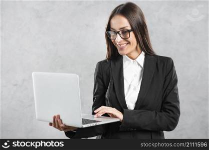 smiling businesswoman looking laptop her hand against concrete wall