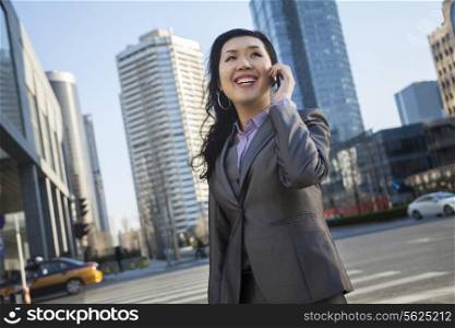 Smiling businesswoman on the phone and looking away in the street in Beijing