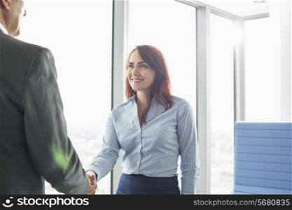 Smiling businesswoman shaking hands with businessman in office