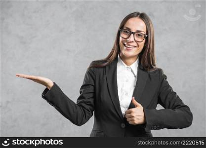 smiling businesswoman showing thumb up sign presenting against gray background