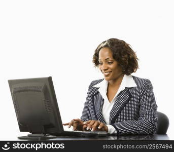 Smiling businesswoman sitting at desk typing on computer.