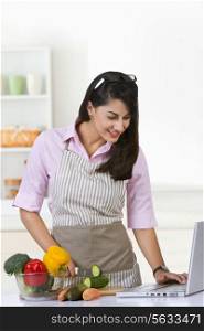 Smiling businesswoman surfing on laptop while preparing food in kitchen at home