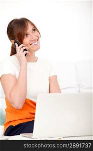 Smiling businesswoman talking on phone and using her laptop sitting on a sofa at home