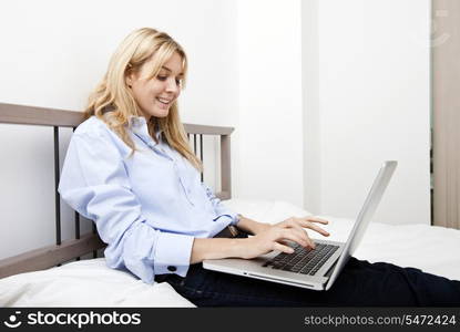 Smiling businesswoman using laptop in bed