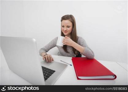 Smiling businesswoman using laptop while drinking coffee in office