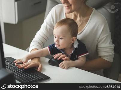 Smiling businesswoman working at computer with baby boy sitting on her lap