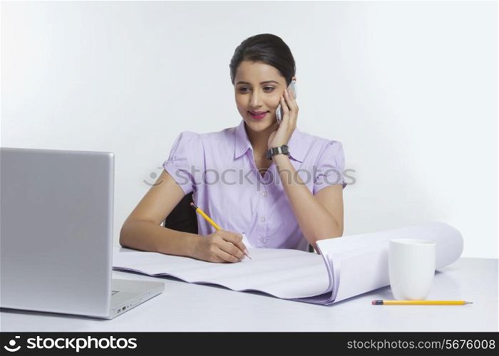 Smiling businesswoman working at desk against white background