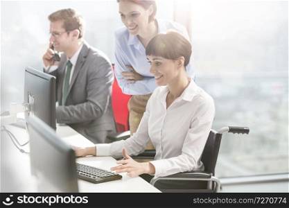 Smiling businesswomen discussing by colleague working at desk in modern office
