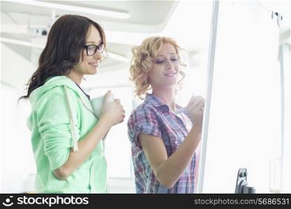 Smiling businesswomen preparing presentation on whiteboard in creative office
