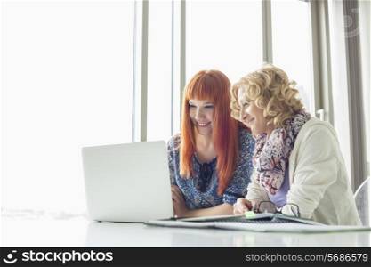Smiling businesswomen using laptop together in creative office