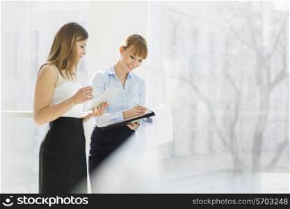 Smiling businesswomen with tablet PC and folder working by railing in office