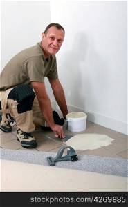 Smiling carpet fitter spreading adhesive on an old tiled floor