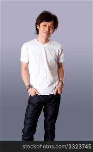 Smiling casual Asian man wearing white shirt and jeans standing with hands in pockets and happy expression, isolated.