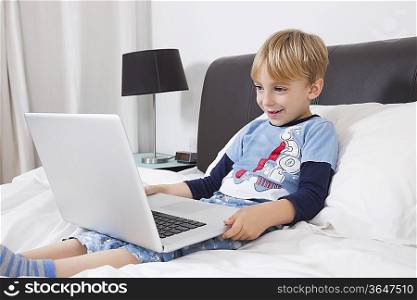 Smiling Caucasian boy using laptop computer in bed