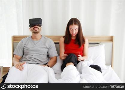 Smiling Caucasian Couplegame love relaxing with Virtual Reality glasses box on tablet in social media online game with mate in bedroom. Technology and Lifestyle of married family on holiday Concept.