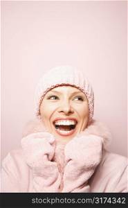 Smiling Caucasian mid-adult woman on pink background wearing winter coat and hat.