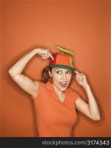 Smiling Caucasian mid-adult woman pointing and wearing propeller cap on orange background.