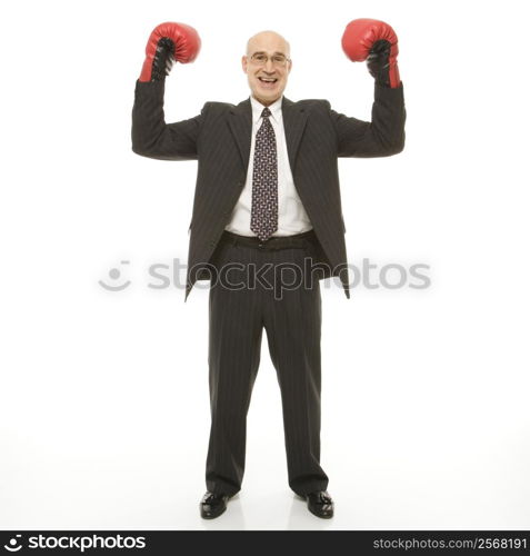 Smiling Caucasian middle-aged businessman standing with arms raised wearing boxing gloves.