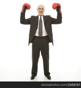 Smiling Caucasian middle-aged businessman standing with arms raised wearing boxing gloves.
