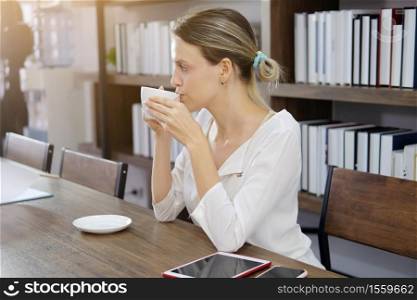 Smiling Caucasian woman happy with smell the aroma of hot coffee in modern cafe. She is relaxing with social online on tablet and smartphone on holiday. Lifestly and technology concept