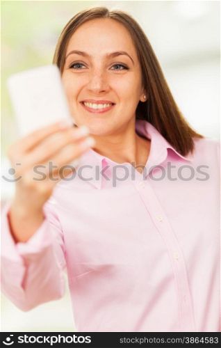 Smiling caucasian woman with pink shirt is doing a selfie with her phone