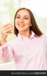 Smiling caucasian woman with pink shirt is doing a selfie with her phone