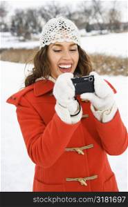 Smiling Caucasian young adult female in winter clothing using digital camera outdoors.