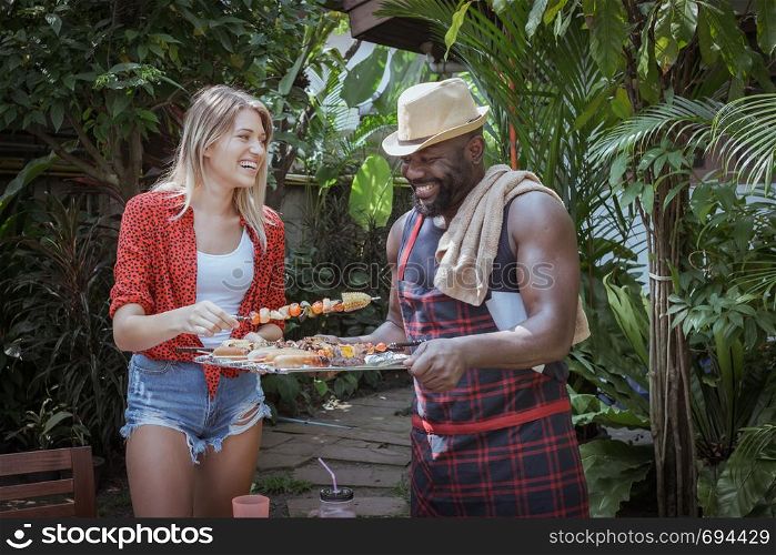 Smiling chef give barbecue to female friend for dinner camping in nature outdoor as summer lifestyle