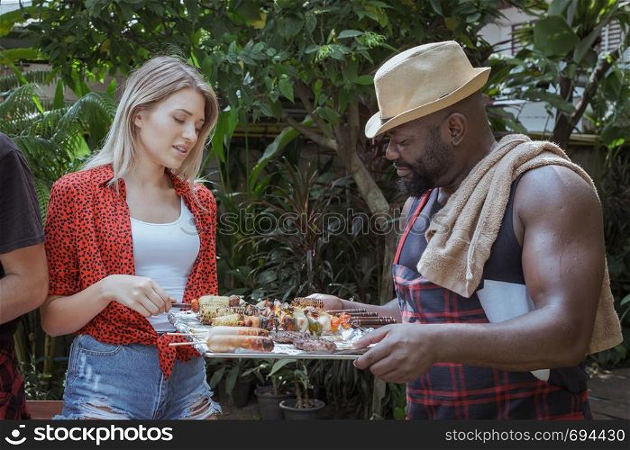 Smiling chef give barbecue to friend for dinner camping in nature outdoor as summer lifestyle